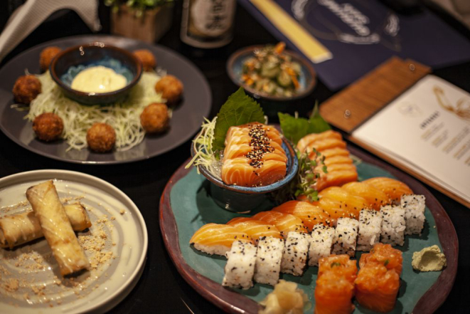 Ao fundo, bolinho de salmão e porção de sunomono (pepino em conserva agridoce). À frente, harumaki (rolinho primavera) e o combinado Gurumê médio (R$ 100, 32 peças, o sashimi pode ser de atum, salmão e peixe branco). Foto: Rodrigo Augusto Zerbien/Divulgação