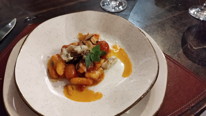 Cavatelli de bacalhau, com molho exclusivo defumado, tomates e azeitonas azapa e finalizado lascas de bacalhau marinadas em azeite extra virgem, com lâminas de alho frito.