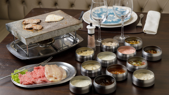 Fondue na pedra com filé mignon e frango (são 300g de carnes por pessoa, sendo 150g de cada variedade), acompanhado de 13 variedades de molhos, do Château de Gazon.