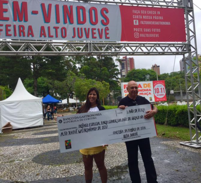 Franciele retira o prêmio das mãos de Maurício Marques, organizador do evento. Ela vai poder comer de graça em todas as edições da feira Alto Juvevê em 2017. Foto: Divulgação.