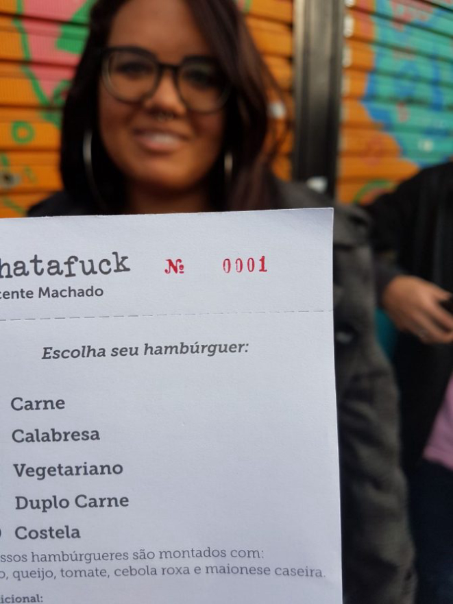 A primeira cliente da fila exibe a senha número 1 para retirar o novo hambúrguer de costela do Whatafuck. Foto: Guilherme Requião.