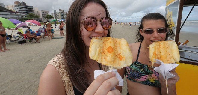 As primas Keity Pinheiro, 18, e Bruna Pinheiro, 16, não resistiram ao cheirinho do crepe que o vizinho de guarda-sol comprou. Foto: Albari Rosa / Gazeta do Povo.