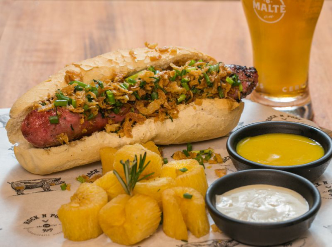 Sanduiche Rock n´Pork do Clube do Malte Juvevê (linguiça campeira artesanal, molho caseiro de alho ou mostarda e mel, vinagrete da casa, cebolas crispys e cheiro verde servido no pão baguete especial). Foto: Divulgação.