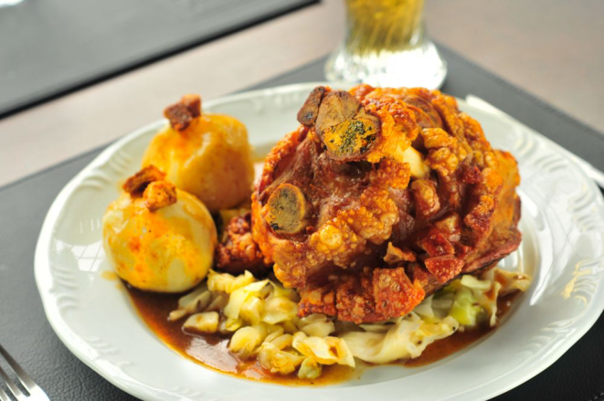 Joelho de porco assado à pururuca acompanha dois bolinhos de batata, chucrute, repolho roxo e salsicha Bratwurst. Serve duas pessoas (R$ 97,90). (Foto: Divulgação)