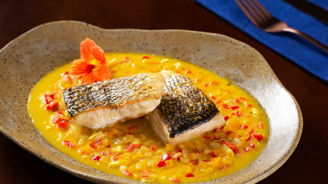 O molho de pimentões, leite de coco e curry no fundo do prato e os pedaços de robalo, grelhados, por cima. / Guardanapo, da Carola Home (@carolahomebr).