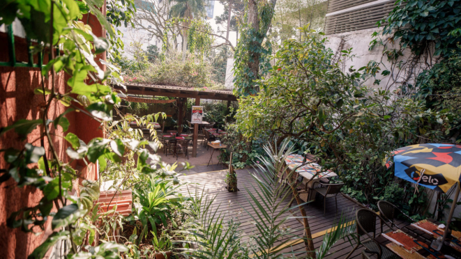 O jardim encantado do Quintana, com mesas entre árvores, arbustos, ervas, frutíferas e colmeias.