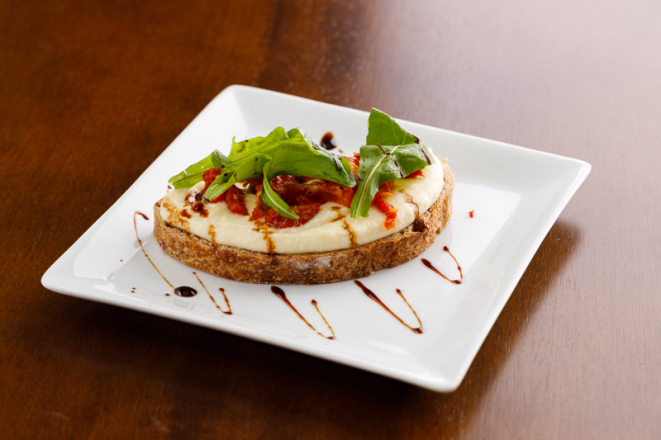 Bruschetta com creme de queijo emmental, tomate seco e rúcula: entrada vegetariana do Vindouro.