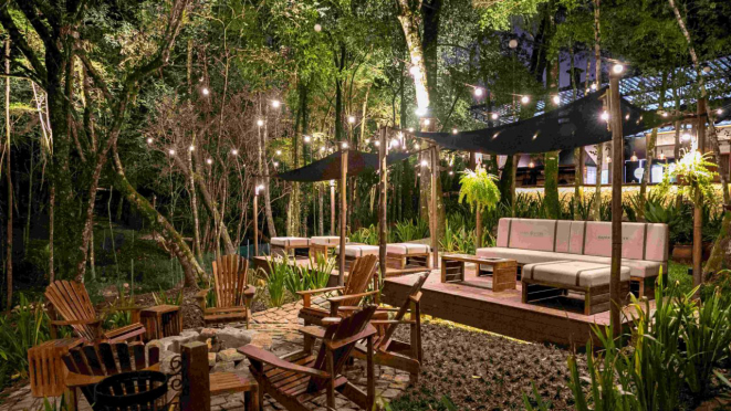 Mesas entre as árvores, para dar um ar de piquenique e das coisas do bosque.