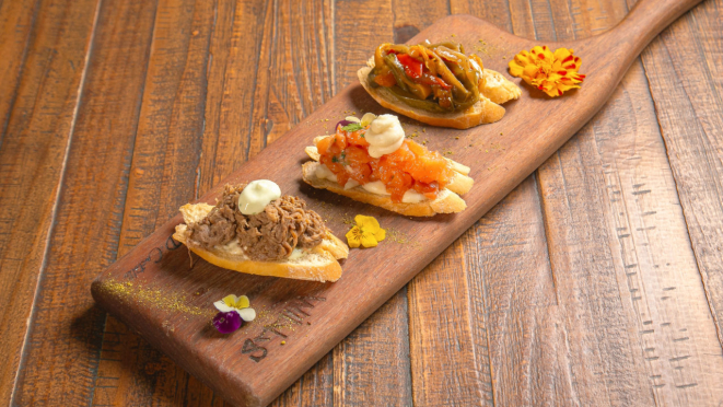 O Wills Cais serve, na entrada, salmão fresco, carne de panela e caponata, sobre pão artesanal, com molho de queijos e maionese verde, finalizada com uma pitada de flor de sal e salsa fresca.