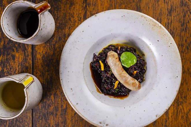 <em>Linguiça de jacaré, acompanhada por salada de arroz selvagem e demi-glace de jacaré com tucupi</em>, uma das entradas do jantar de nove tempos do Maria Eugênia. | Foto: Rodrigo Pierrot