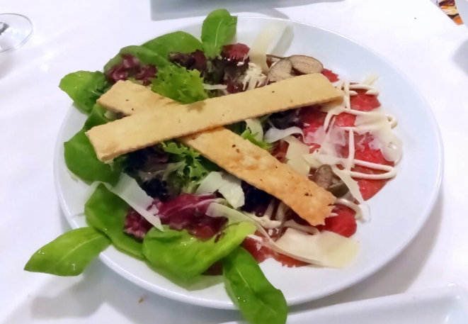 Carpaccio de mignon ao molho de mostarda e mel, acompanhados de alcaparrones, lascas de parmesão, rúcula e pão folha. | Foto: Anacreon de Téos