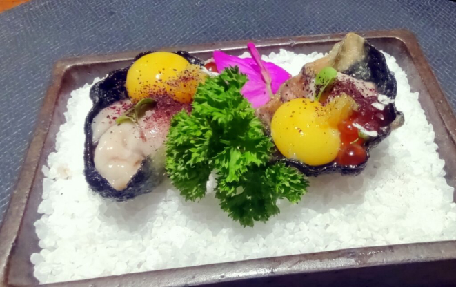 Ostra para degustar com a concha, temperada com flor de sal, ovas com yuzu, gema de codorna e ikura e, por cima, um pó de hibisco. |Foto: Anacreon de Téos