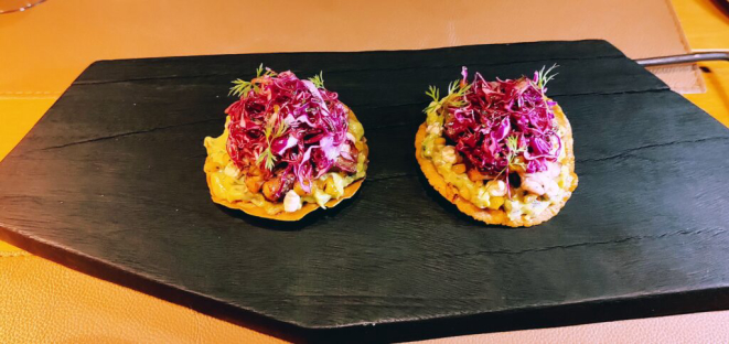 <em>Tostada de polvo</em>, snack composto por polvo braseado, servido sobre tostada crocante, guacamole, milho tostado, emulsão de pimenta chipotle defumada e salada fresca de repolho roxo. | Foto: Anacreon de Téos