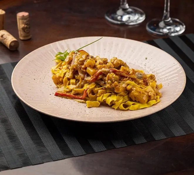 Ragu de bacalhau com cebola roxa e pimentões coloridos, fettucine artesanal com molho tandori e crocante de alho poró.