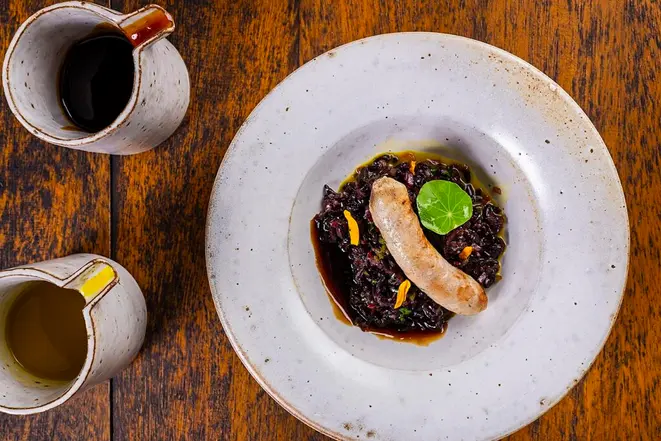 <em>Linguiça de jacaré, acompanhada por salada de arroz selvagem e demi-glace de jacaré com tucupi</em>, uma das entradas do jantar de nove tempos do Maria Eugênia. | Foto: Rodrigo Pierrot