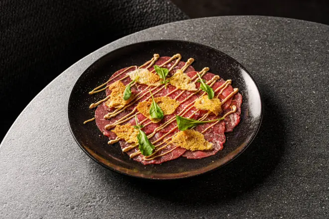 <em>Carpaccio de Wagyu com crocante de parmesão e rúcula</em>, uma das entradas. | Foto: Rubens Kato