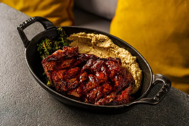 <em>Bife chorizo M2 grelhado</em>, servido com homus de grão-de-bico com cebola caramelizada e brócolis tostado. | Foto: Rubens Kato